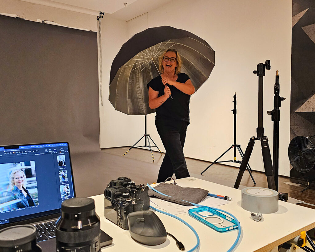 Fotografin lacht im Fotostudio mit Lichtschirm und sorgt für eine gute Atmosphäre am Set